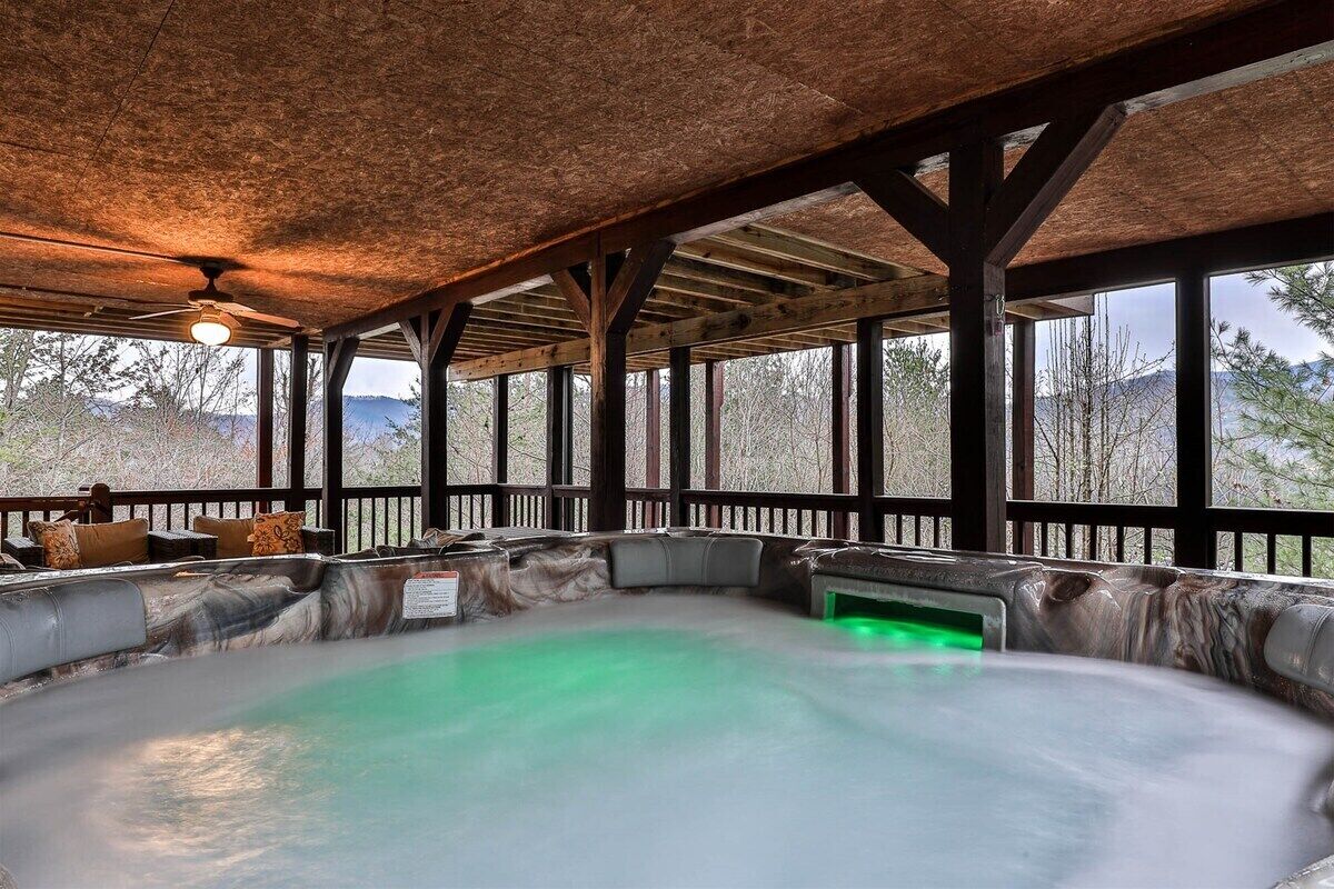 Un bain à remous avec un éclairage vert, des poutres en bois et une vue sur les arbres et les montagnes.