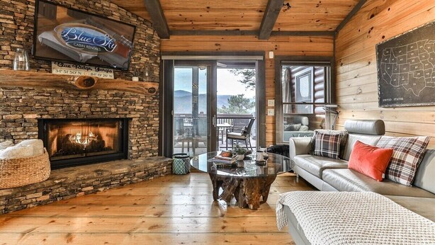 A cabin with a stone fireplace, a wooden ceiling, a glass coffee table, and a sofa with plaid cushions. - Cherry Log Sky Bear | Cherry Log, GA (Blue Ridge)