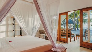 A room with a bed, a chair, a fan, and a view of a beach. - Kijani Beach Villas (Bwejuu)
