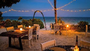 An outdoor dining area with tables and chairs, string lights, and a view of the ocean. - Kijani Beach Villas (Bwejuu)