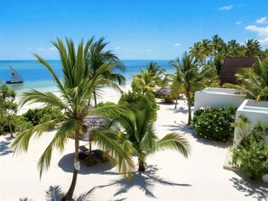 Um resort à beira-mar com palmeiras, uma cabana de palha e um barco na água.