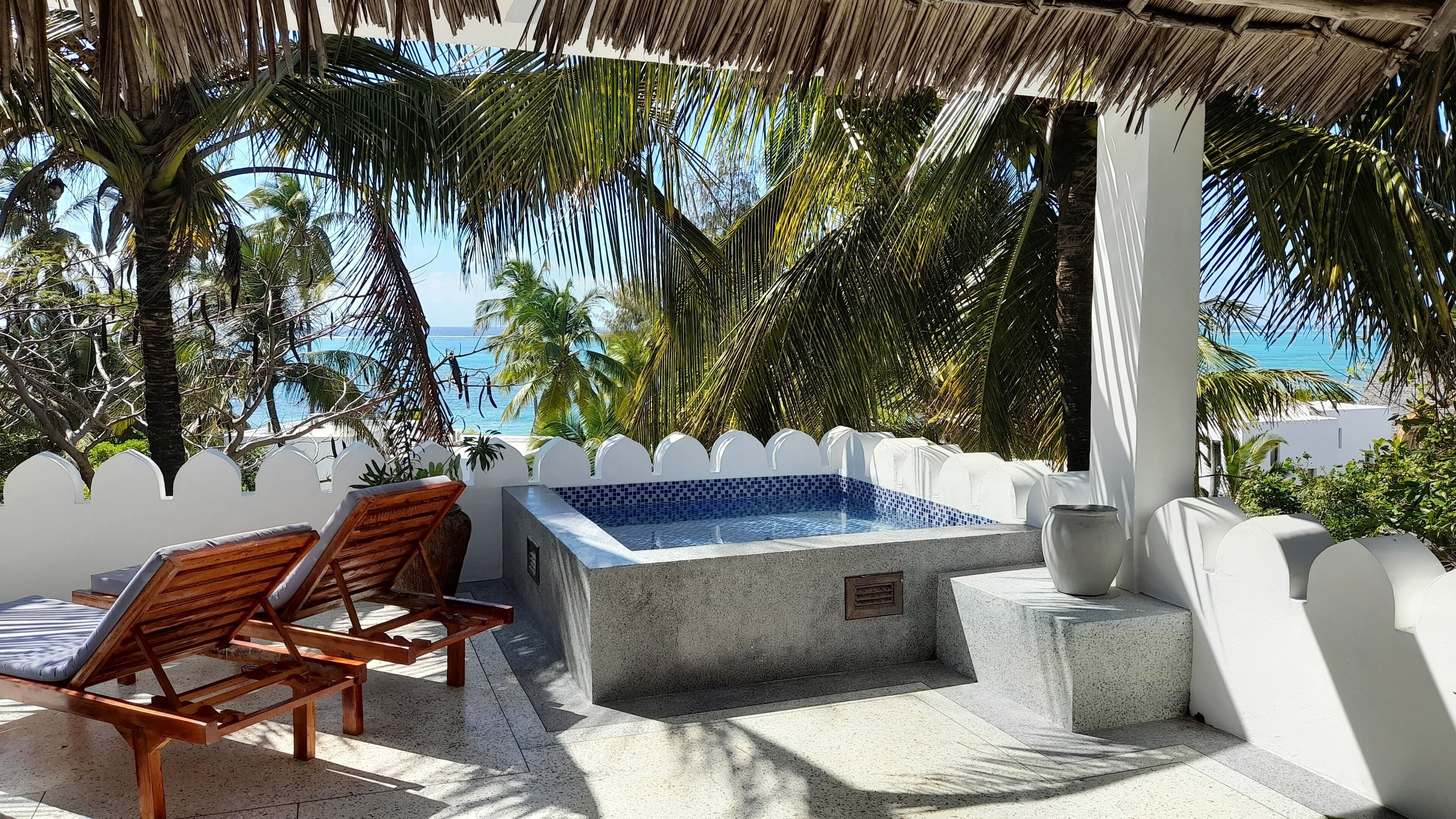 Zona de piscina con un jacuzzi, sillones de madera y vista al océano.