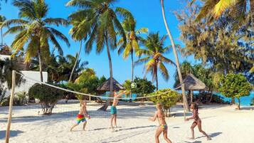 A beach volleyball game on a sandy court surrounded by palm trees and a clear blue sky.