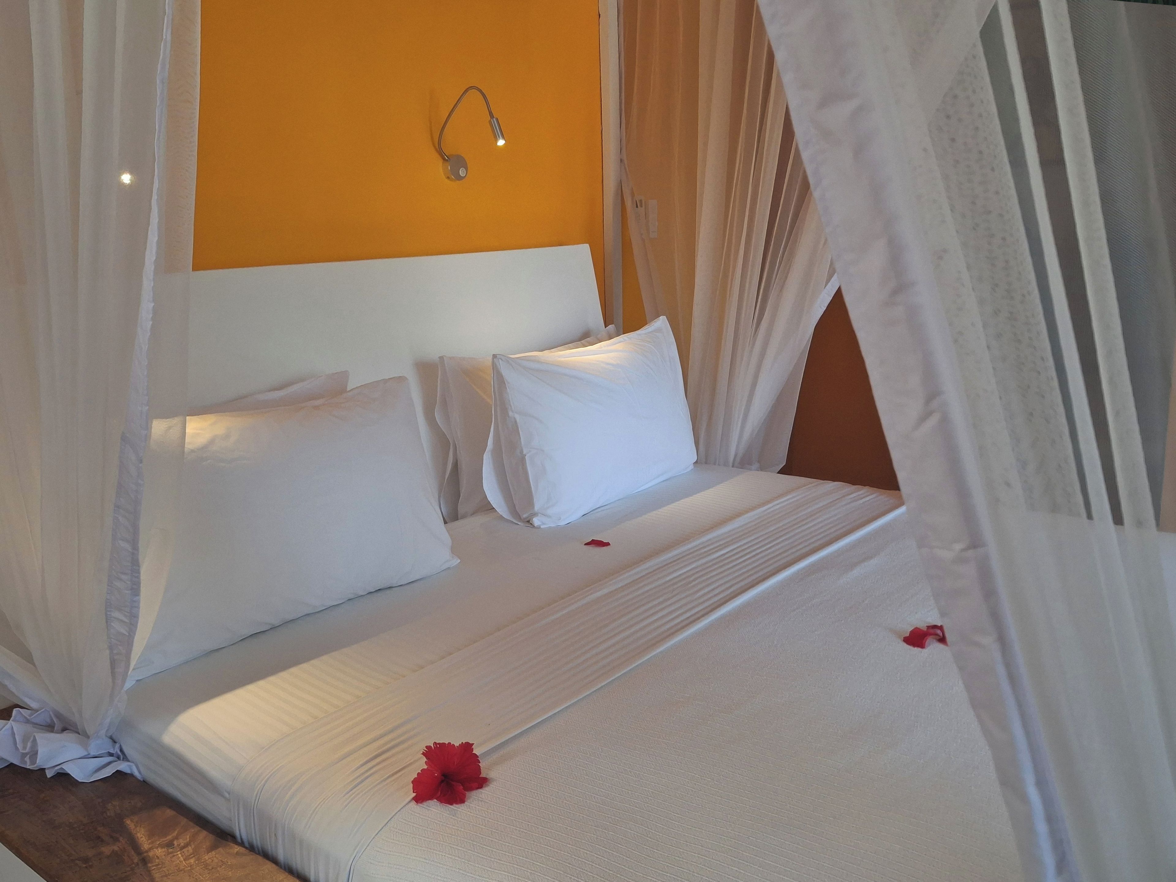 Una cama con ropa de cama blanca, dosel e lámpara fijada a la pared.