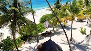 A beach with palm trees, a thatched hut, and a lounge area. - Kijani Beach Villas (Bwejuu)