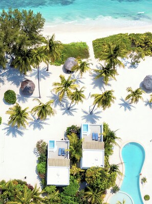 Um resort com duas vilas na praia, uma piscina e vegetação tropical exuberante.