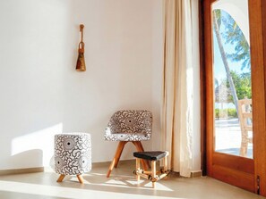 A room with a wooden door, a patterned chair, a small ottoman, and a wall-mounted light fixture. - Kijani Beach Villas (Bwejuu)