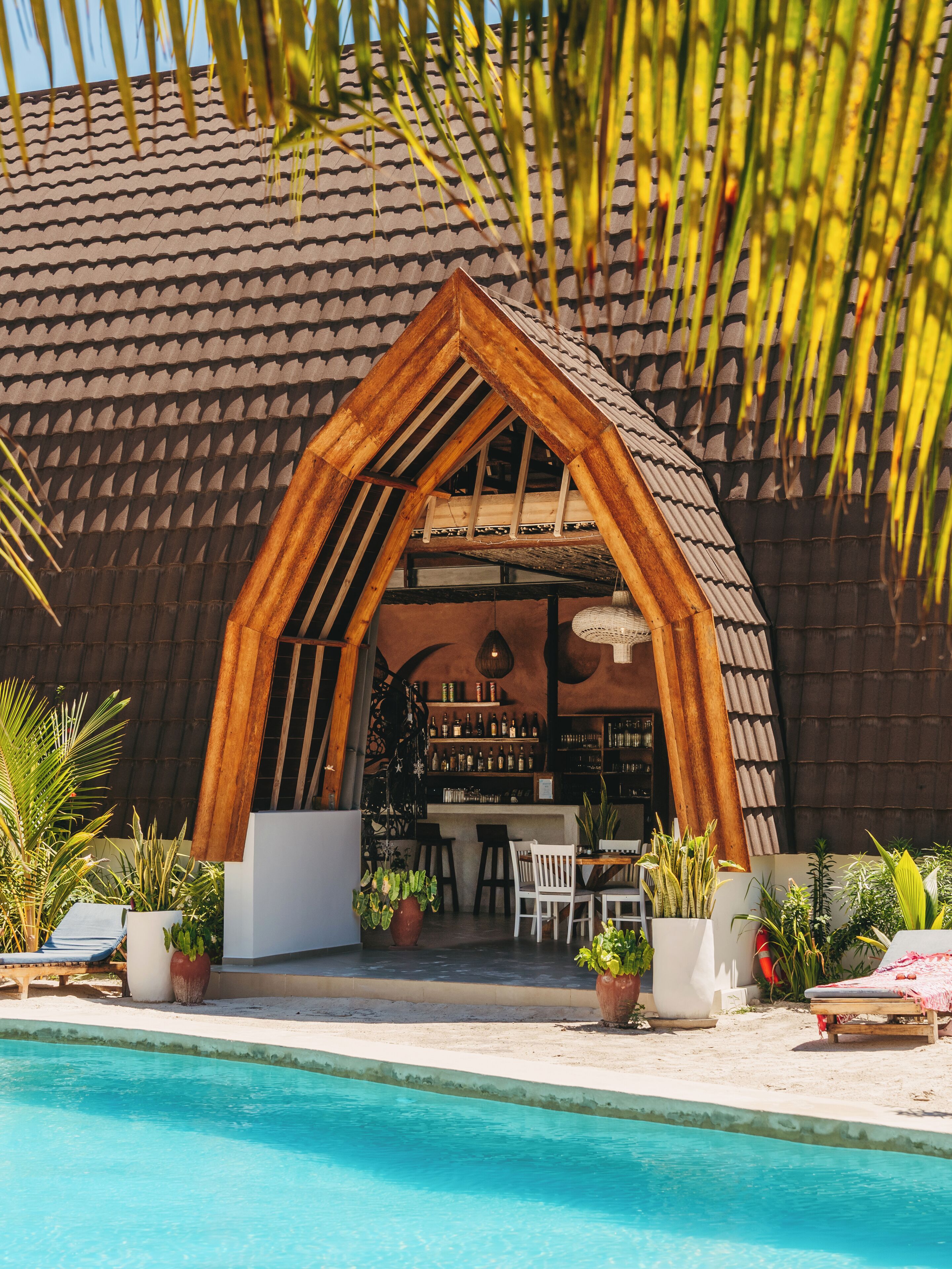 Un área junto a la piscina con una estructura de madera, bar, asientos y plantas en macetas.