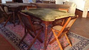 A dining area with a wooden table and chairs, a patterned rug, and a sofa in the background. - Meson Don Quijote (Mota del Cuervo)
