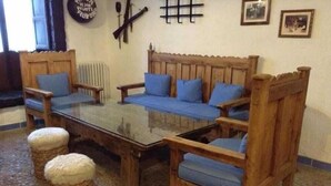 A cozy room with a wooden sofa set, a glass-top coffee table, and two woven ottomans. - Meson Don Quijote (Mota del Cuervo)