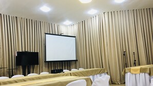 Ein Konferenzraum mit einer großen Projektionsleinwand, weißen Stühlen und einem Tisch mit Tischdecke.