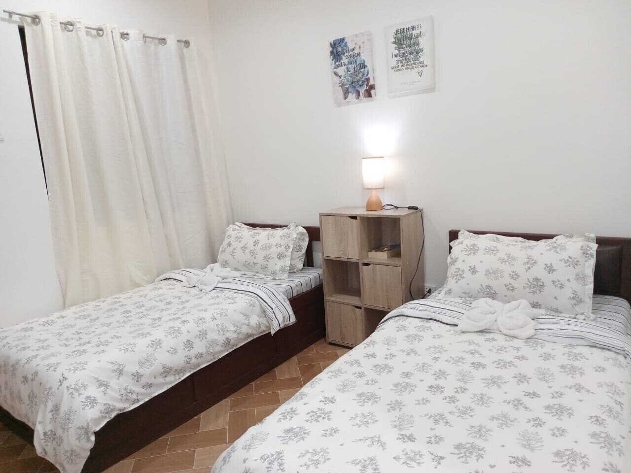 Un dormitorio con dos camas individuales, una mesita de noche con lámpara y un armario de madera.
