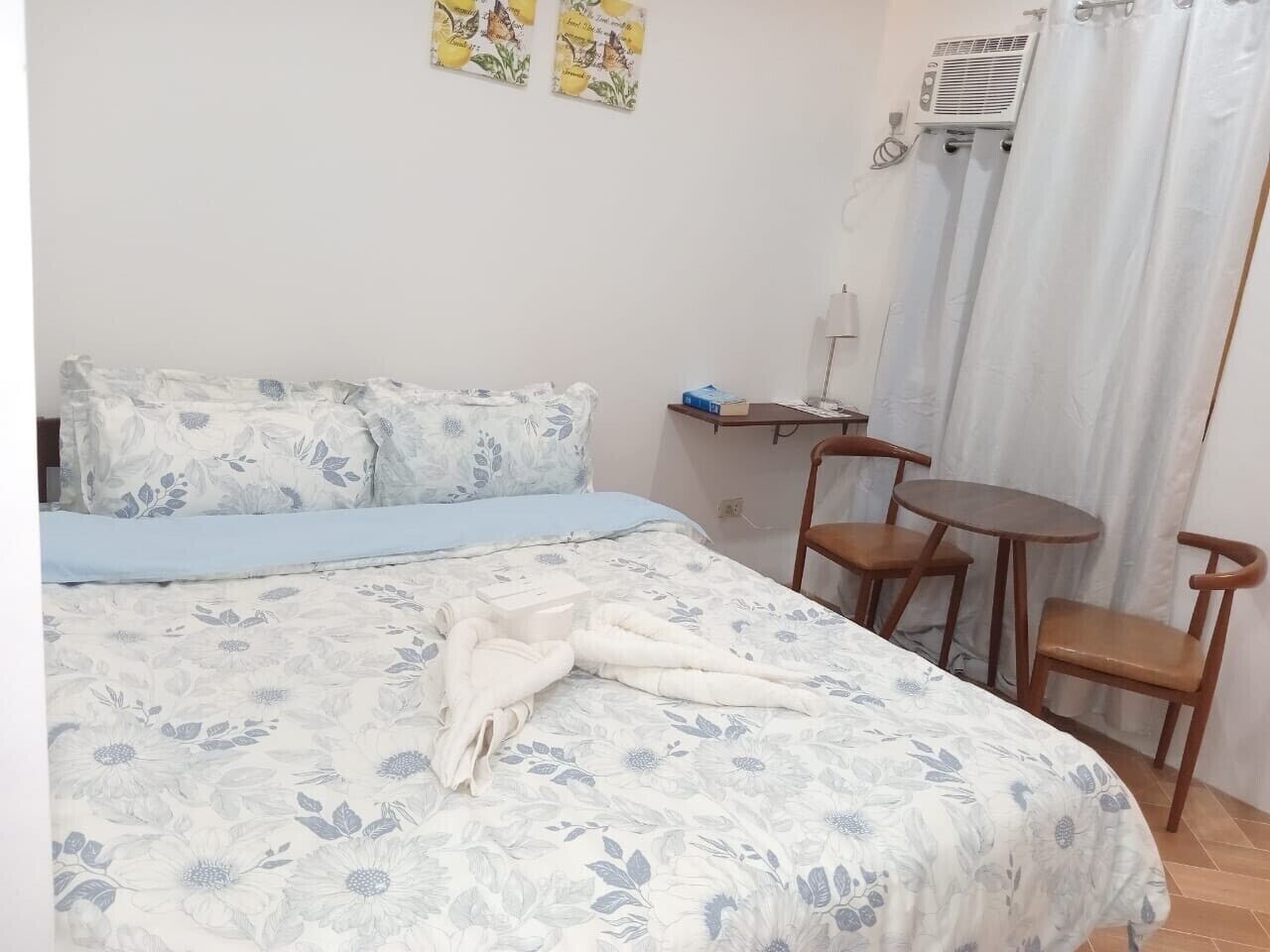 Una habitación de hotel con una cama, una mesita, dos sillas y un aire acondicionado.