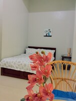 Quarto com cama, uma cadeira de vime e um quadro na parede.
