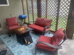 En patio med fletningsmøbler, røde hynder og et bålfællesskab.