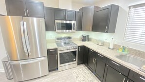 A modern kitchen with stainless steel appliances, dark cabinetry, and a granite countertop. - BonVoyage-Sleep&Sail-OvernightLayovers-Sleeps 8 Near Airport-Cruise Ports (Long Beach)