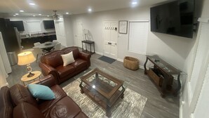 A modern living room with a brown leather sofa, a glass coffee table, and a flat-screen TV mounted on the wall. - BonVoyage-Sleep&Sail-OvernightLayovers-Sleeps 8 Near Airport-Cruise Ports (Long Beach)