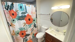 Ein Badezimmer mit Toilette, Waschbecken, Spiegel und einer Duschvorhang mit floralem Muster.