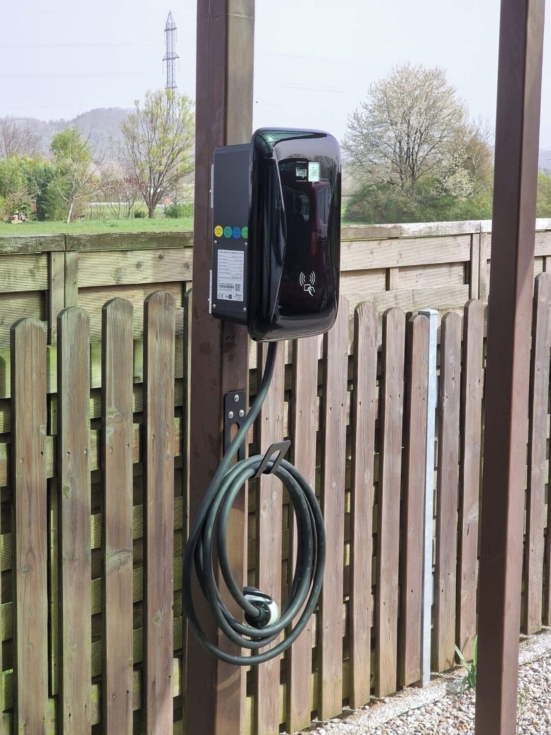 Una estación de carga portátil para vehículos eléctricos instalada en una valla de madera.
