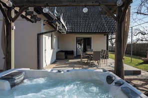 A hot tub in a covered outdoor area with a patio, a table, and chairs. - Jacuzzi, BBQ and EV Charger | 5BR Villa with Garden (Limbuš)