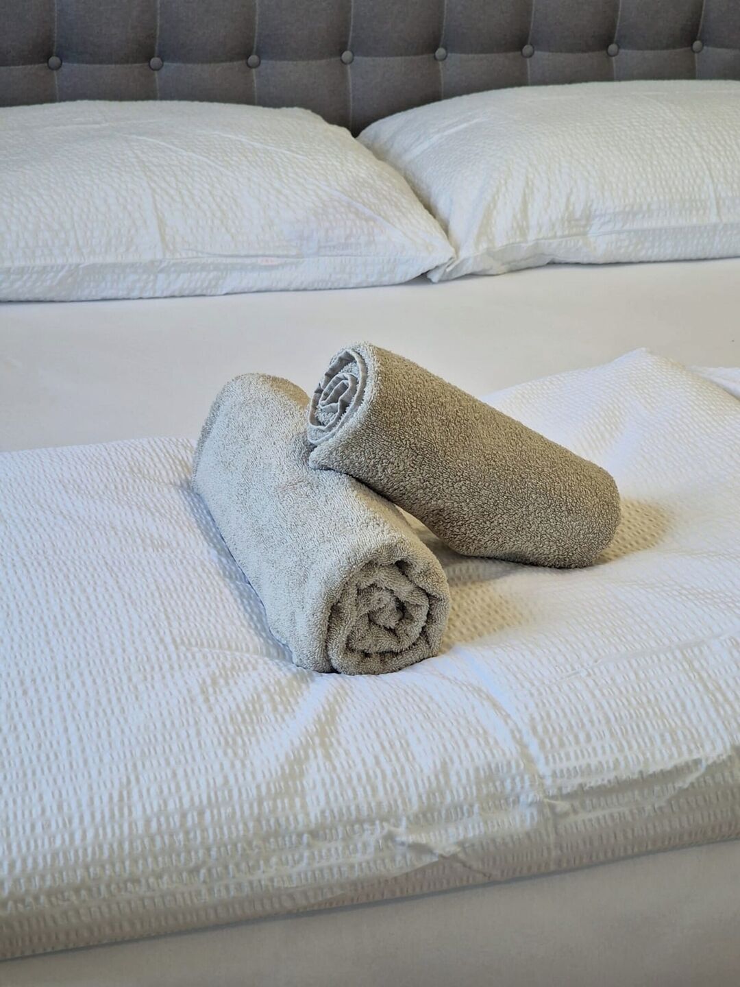 Una cama bien hecha con sábanas blancas y dos toallas enrolladas sobre la cama.