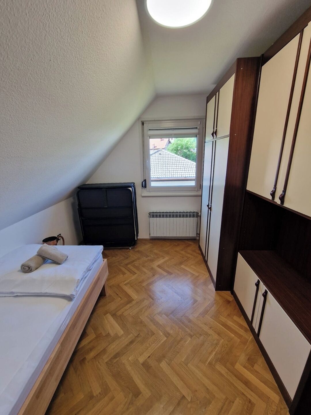 Een kleine, netjes ingerichte kamer met een bed, een radiator, een raam en een kledingkast.