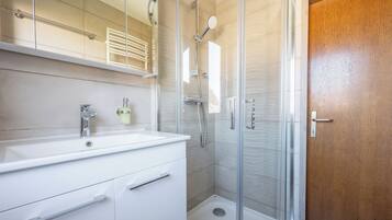 Une salle de bain moderne avec une douche à parois de verre, un lavabo blanc et une porte en bois.