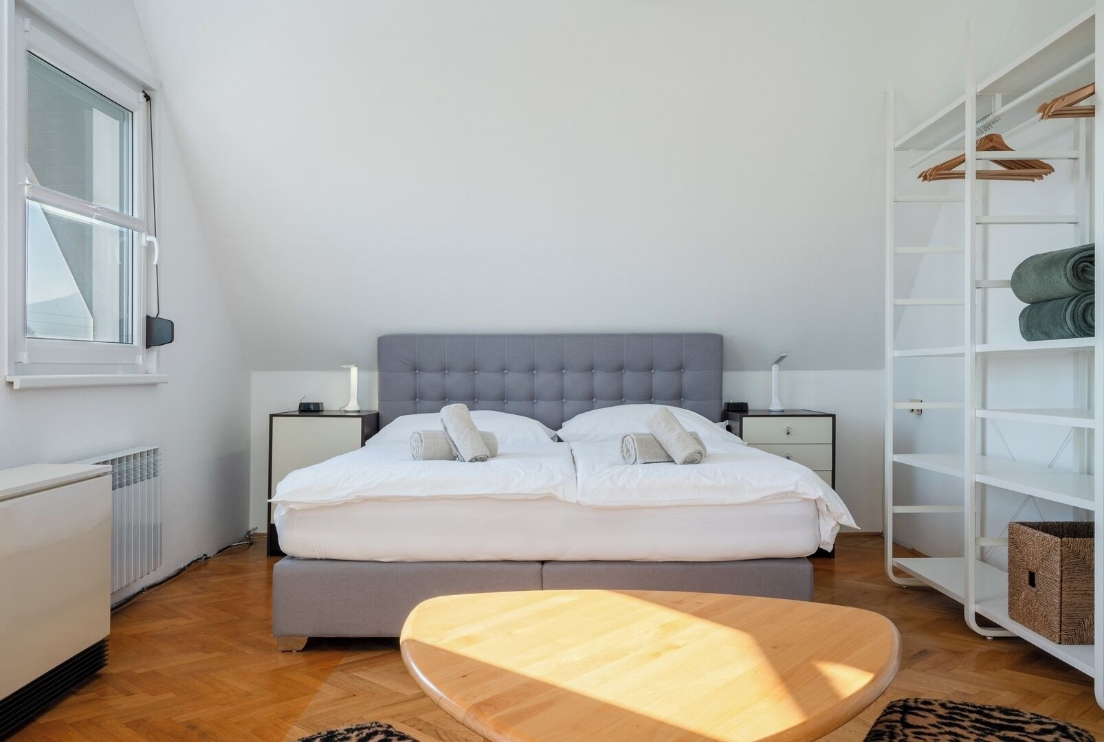 Een slaapkamer met een bed, nachtkastjes, een kledingkast en een houten tafel.
