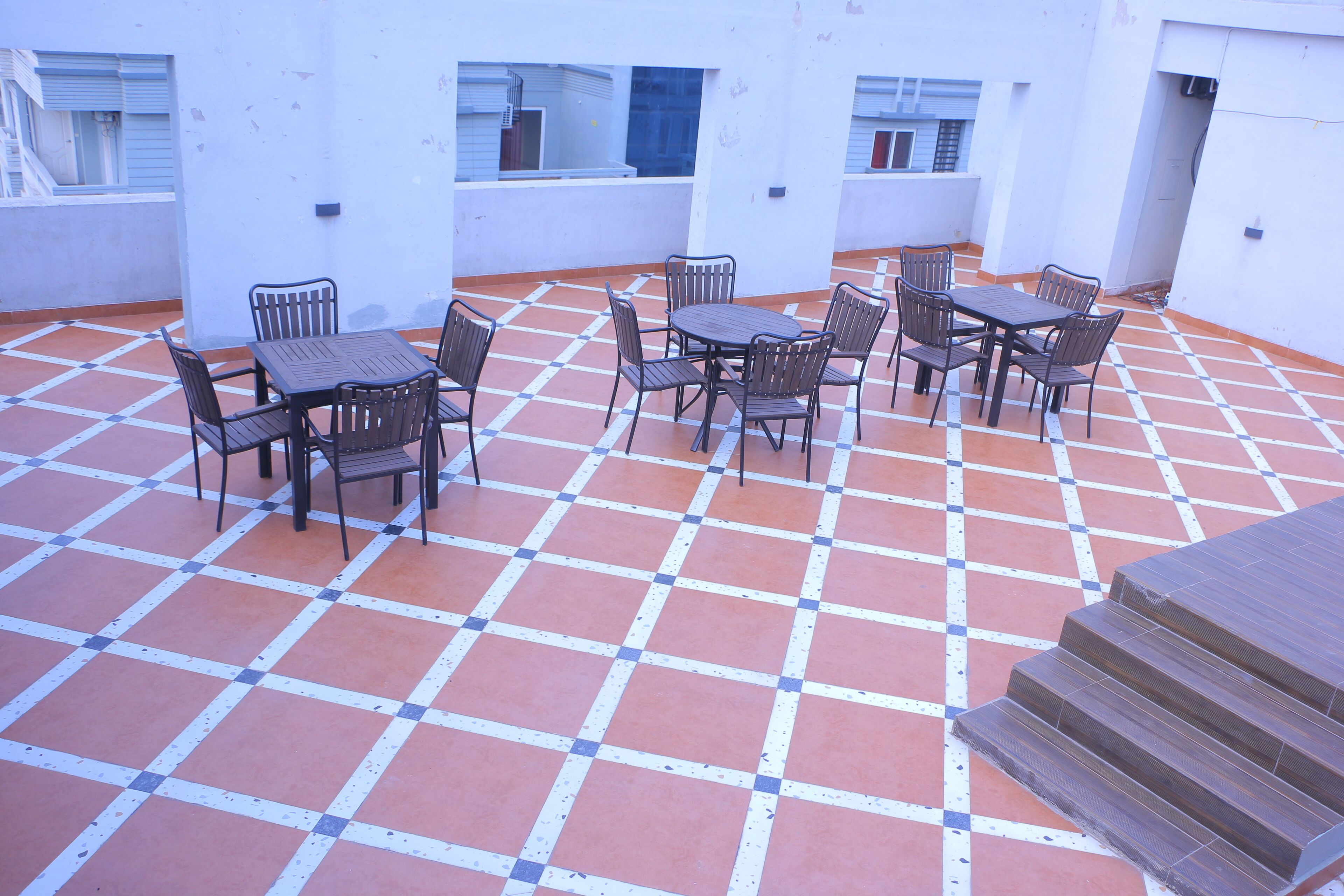 A rooftop terrace with a tiled floor, a table with chairs, and a set of stairs.