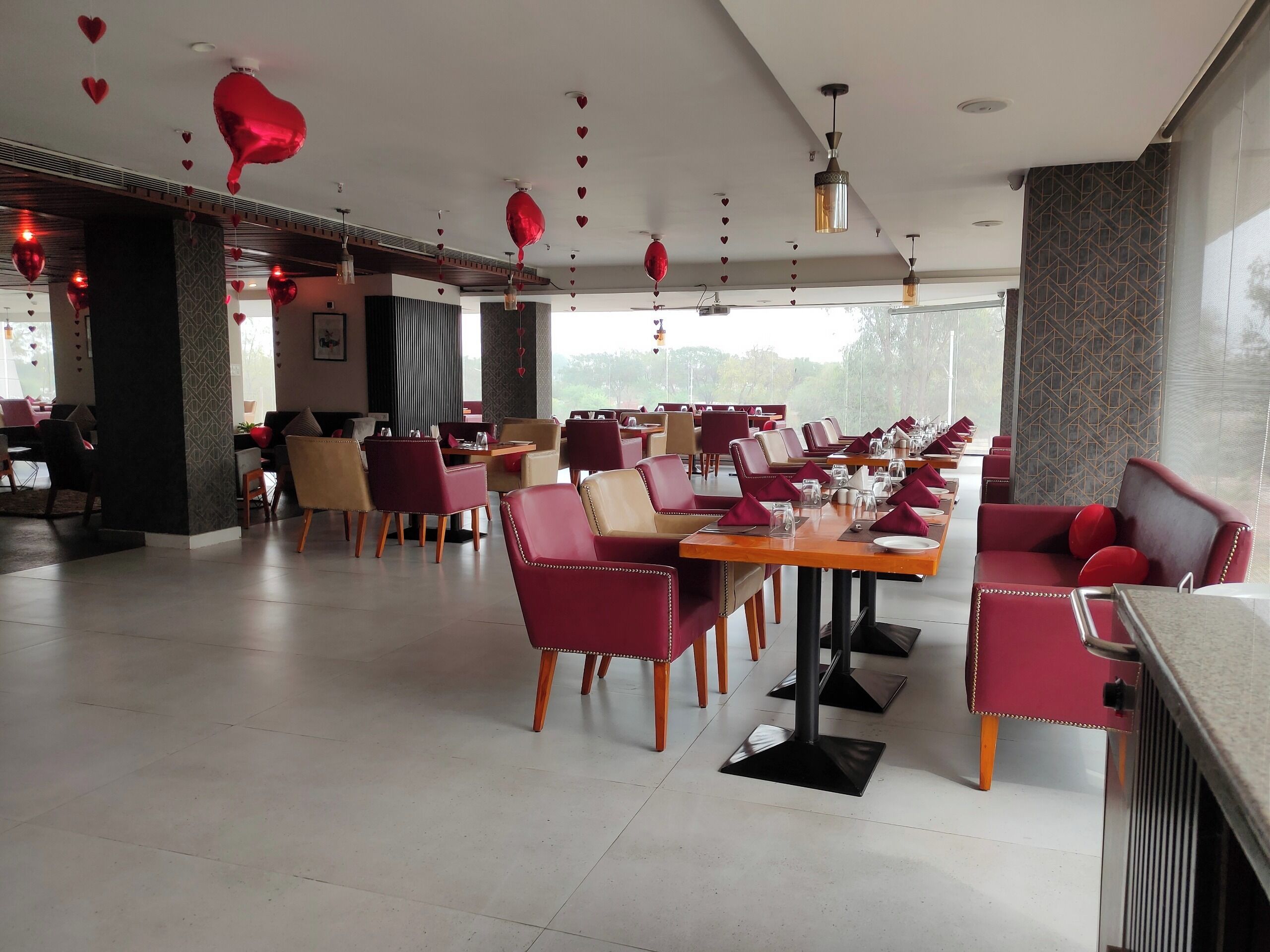 A restaurant with red and beige chairs, tables set with plates, glasses, and napkins.