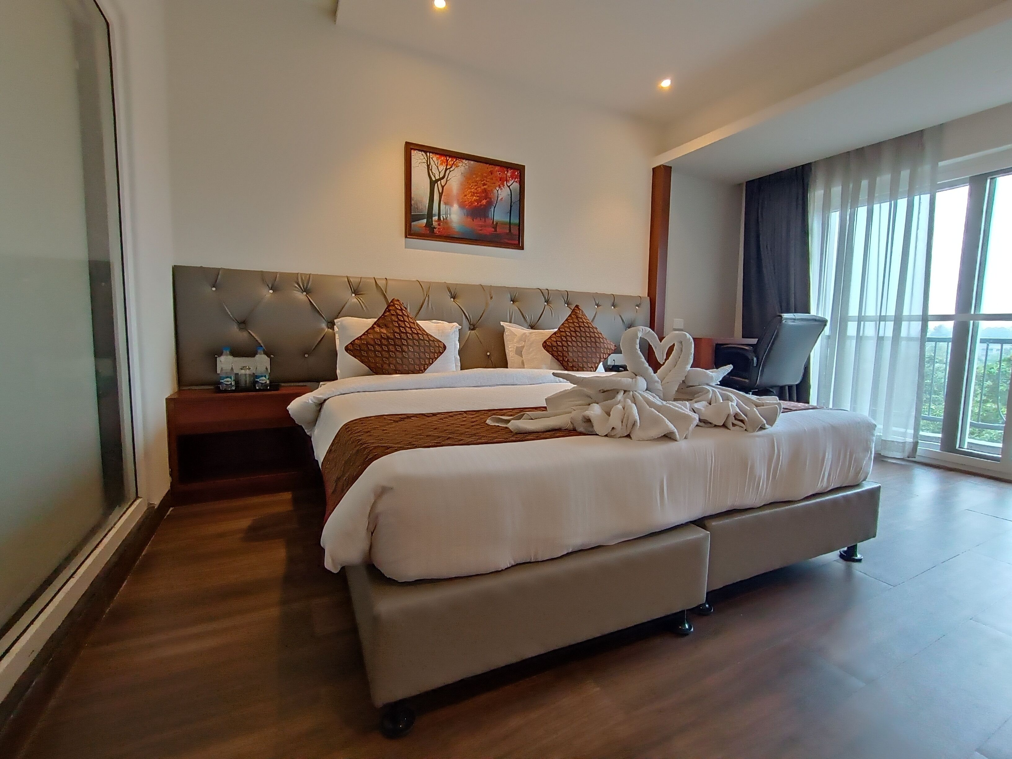 Una cama grande con cabecera, una mesita de noche, una lámpara y un cuadro en la pared.