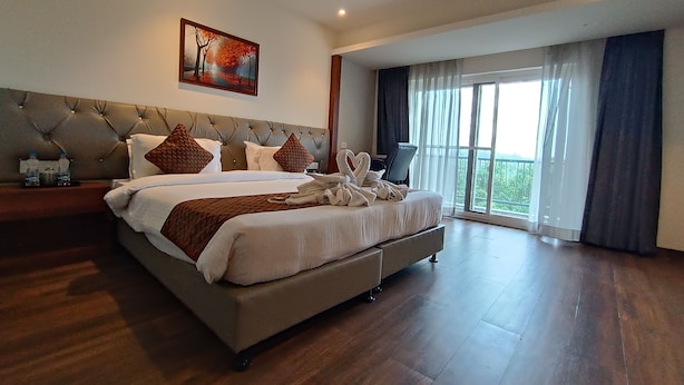 A spacious bedroom with a large bed, a headboard with tufting, a painting above the bed, and a balcony with curtains. - Tulip Arena Hotel Club Event By SGL (Raipur)