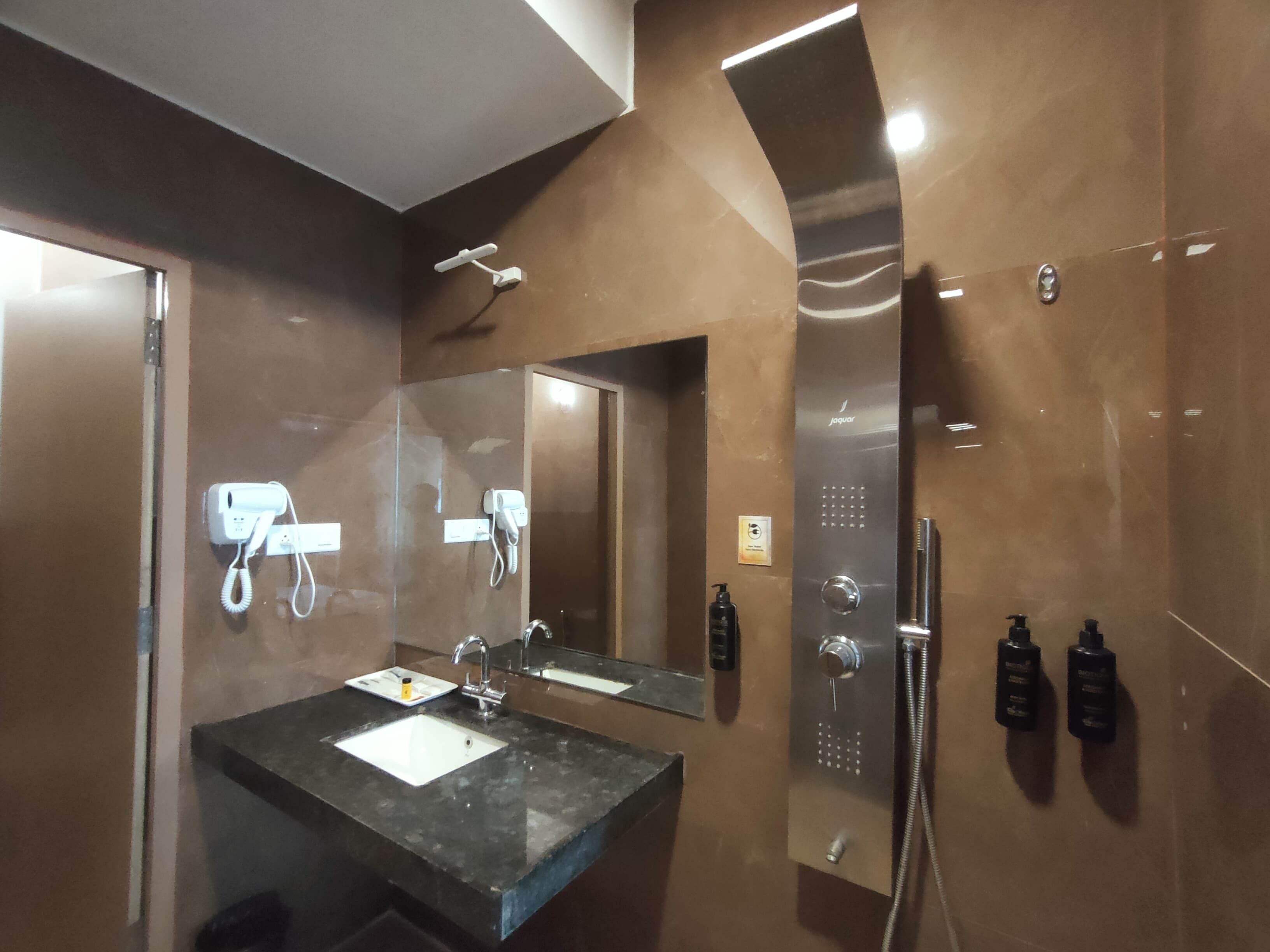 A modern bathroom with a large mirror, two sinks, a shower, and a hairdryer mounted on the wall.