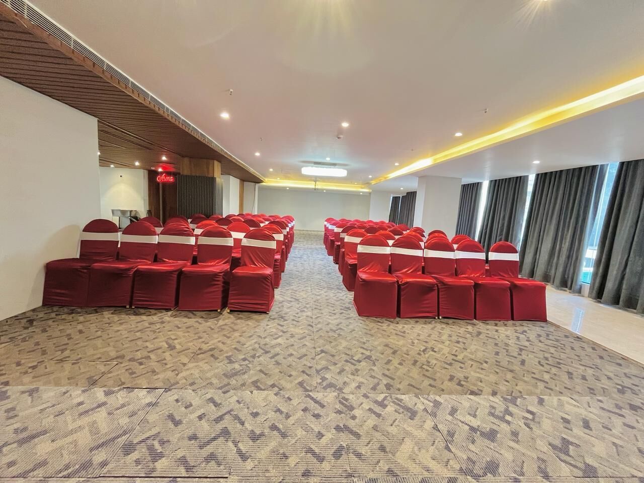 A conference room with rows of red chairs, a patterned carpet, and a modern ceiling design.