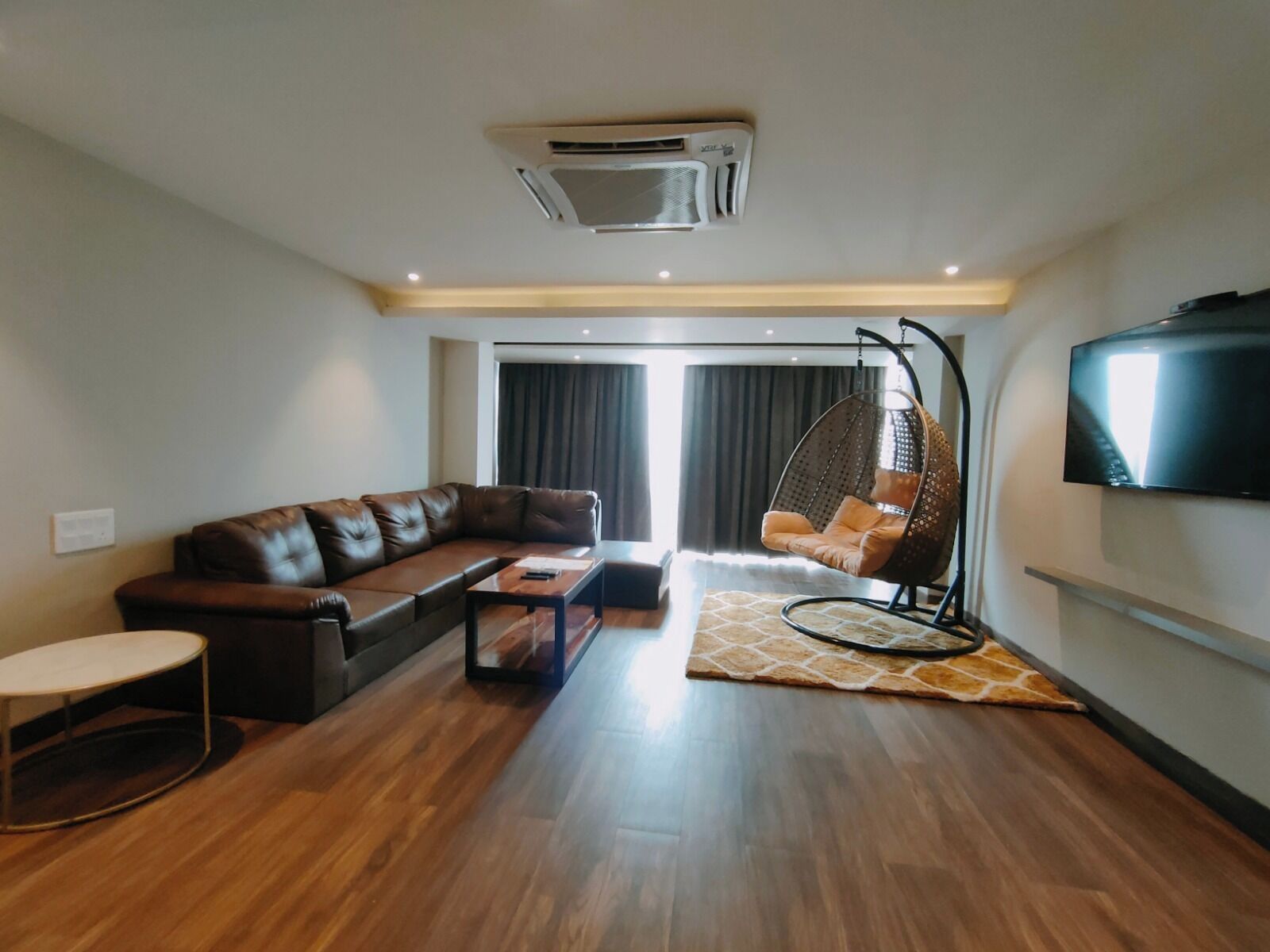 Una sala moderna con un sofá de cuero, una silla colgante, una mesa de centro y un televisor de pantalla plana montado en la pared.