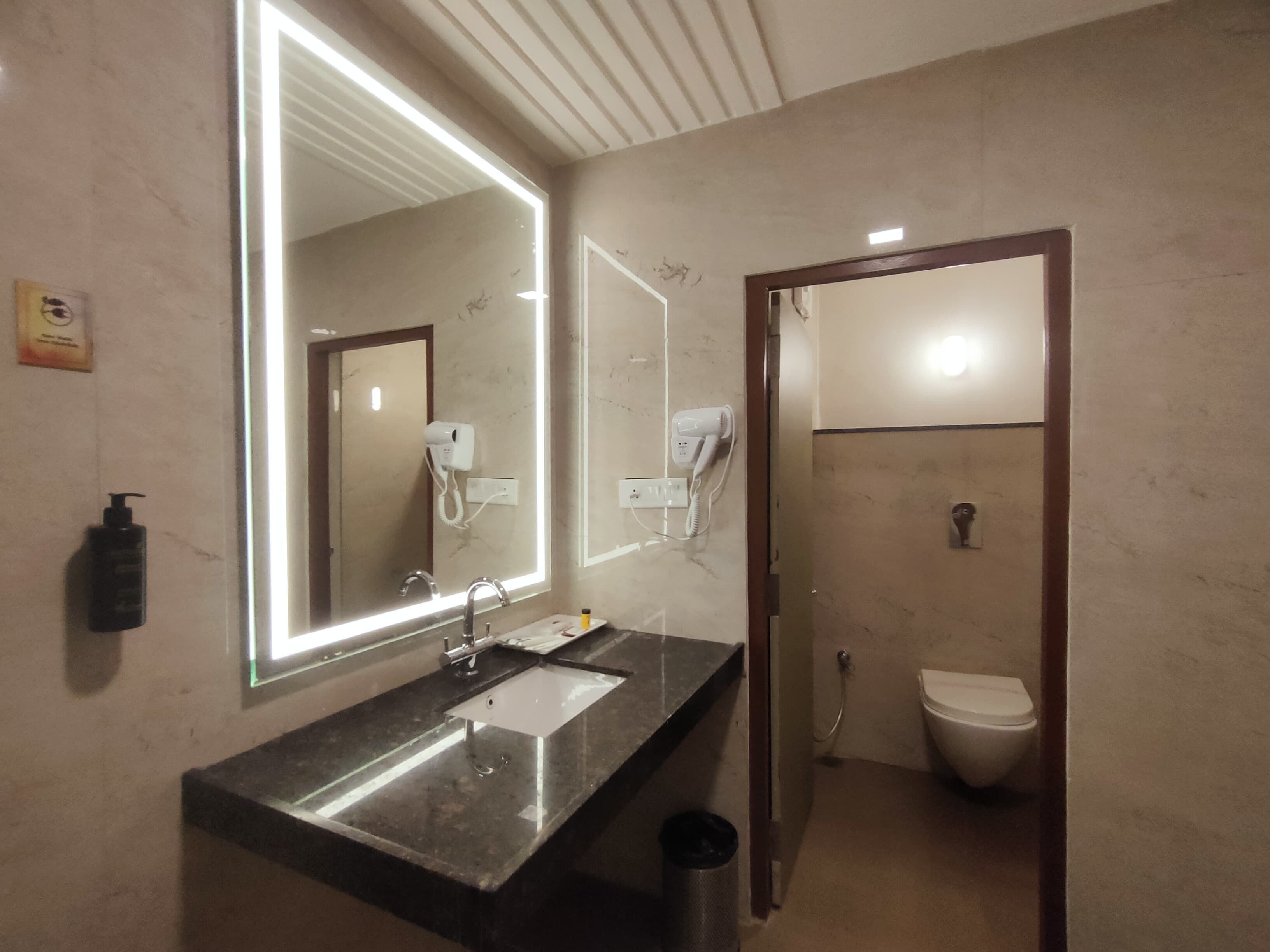 A bathroom with a large mirror, a sink, a hairdryer, and a toilet.