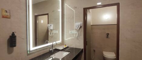 A bathroom with a large mirror, a sink, a hairdryer, and a toilet.