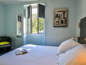 Ein Schlafzimmer mit Bett, Stuhl, einem Fenster mit geöffneten Rollläden und einem an der Wand montierten Telefon.