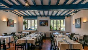 Zona pranzo con diversi tavoli apparecchiati, ampie finestre e un soffitto rustico con travi a vista.