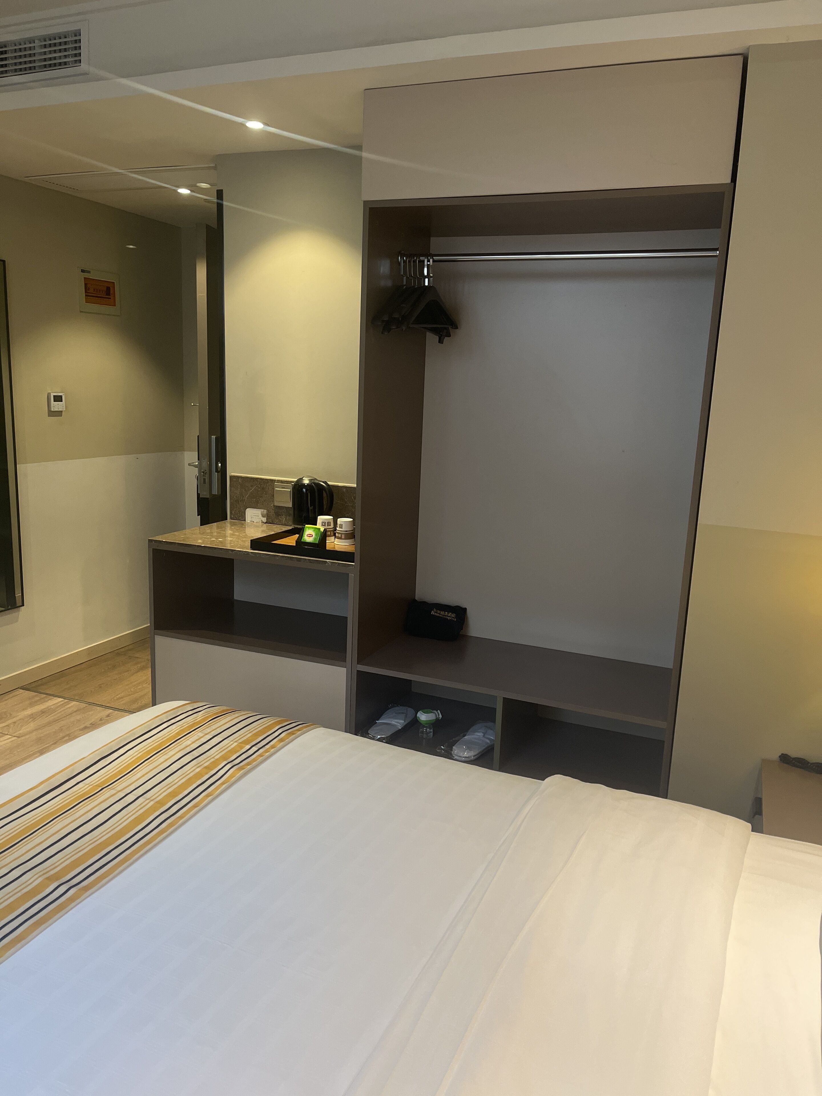 A hotel room with a bed, a vanity with a mirror, a small kitchenette, and a wardrobe.