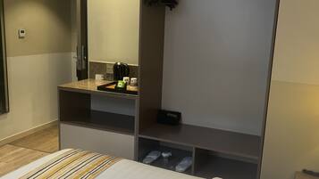 A hotel room with a bed, a vanity with a mirror, a small kitchenette, and a wardrobe.