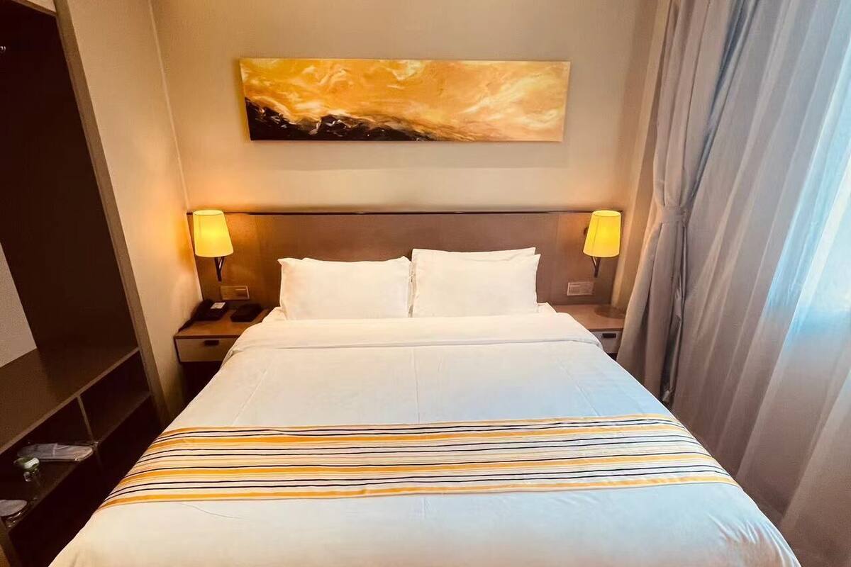 A large bed with a striped bedspread, two bedside lamps, a headboard, and a painting above the bed.