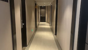 A long, narrow hallway with a tiled floor, doors on both sides, and a ceiling with recessed lighting and a security camera. - Home Inns Collection Hotel (Shanghai)