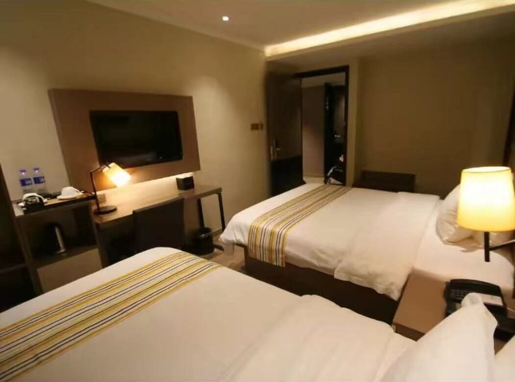 Een hotelkamer met twee bedden, een televisie, een bureau met lamp en een telefoon.