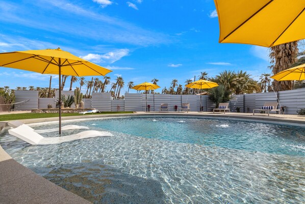 A swimming pool with clear water, surrounded by palm trees and yellow umbrellas.
