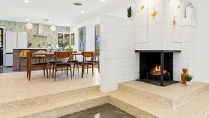 A modern kitchen with a dining area, a fireplace, and a staircase leading to an upper level. - The Long Ranch - Sprawling 1 acre Horse Park Hideaway (Thermal)