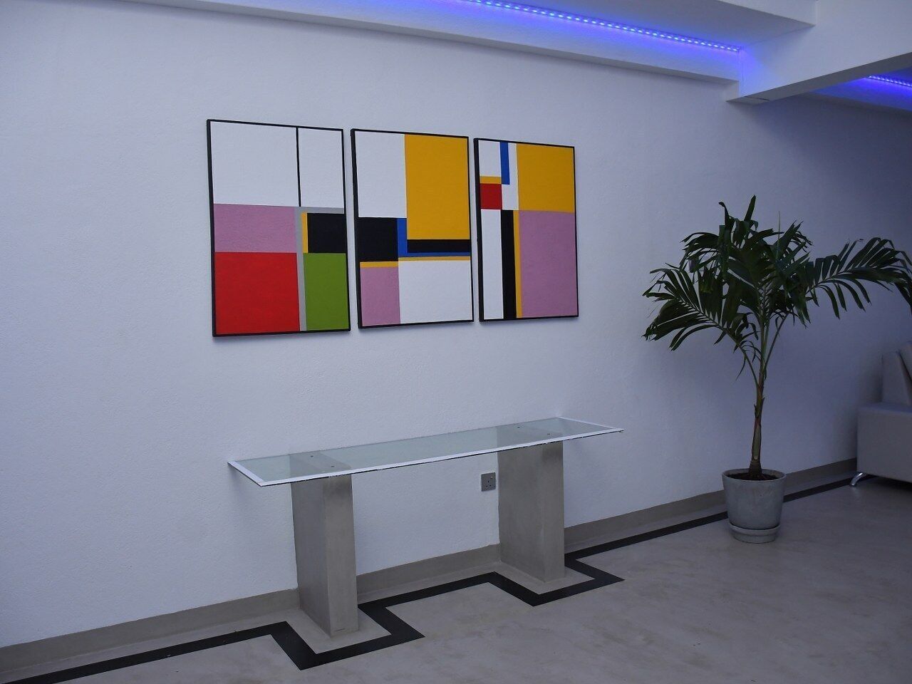 A modern interior with a white bench, a potted plant, and abstract art on the wall.