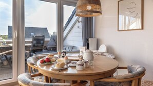 Ein Essbereich mit einem runden Holztisch, gemusterten Stühlen und einer Korbtreleuchte.
