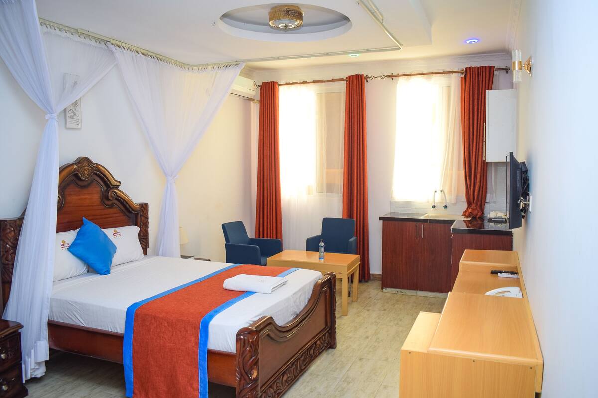 Une chambre d’hôtel avec un lit en bois, un bureau, une chaise, une télévision et une salle de bain.