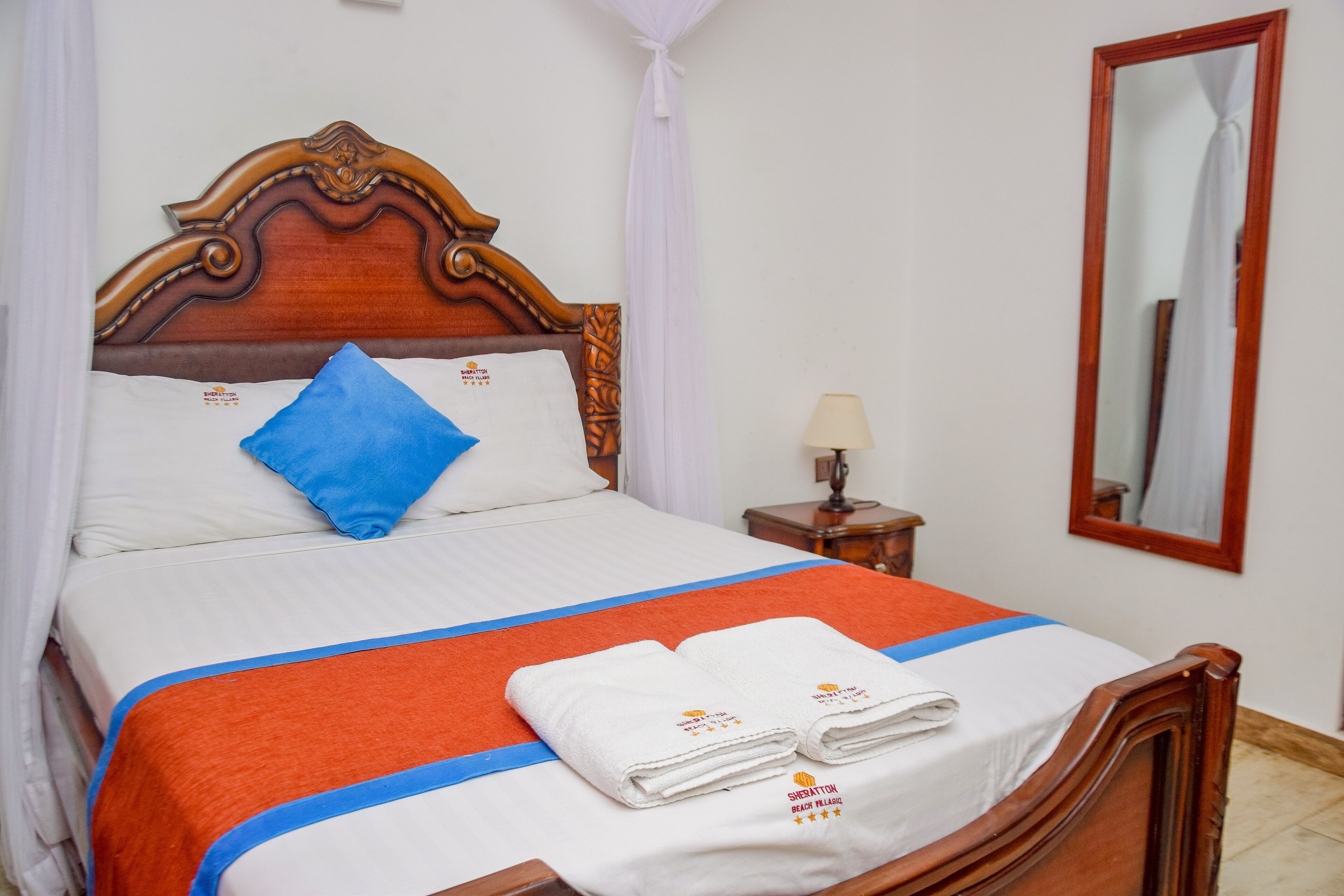 A neatly made bed with a wooden headboard, white and blue bedding, and two folded towels with a logo.